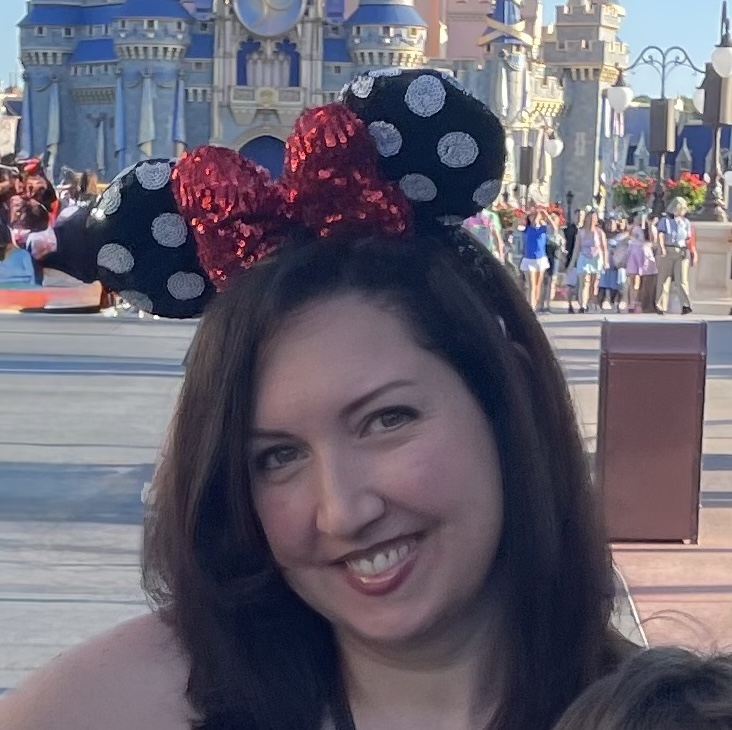 Diana Tombolillo smiling while wearing Minnie Mouse ears in front of Cinderella Castle