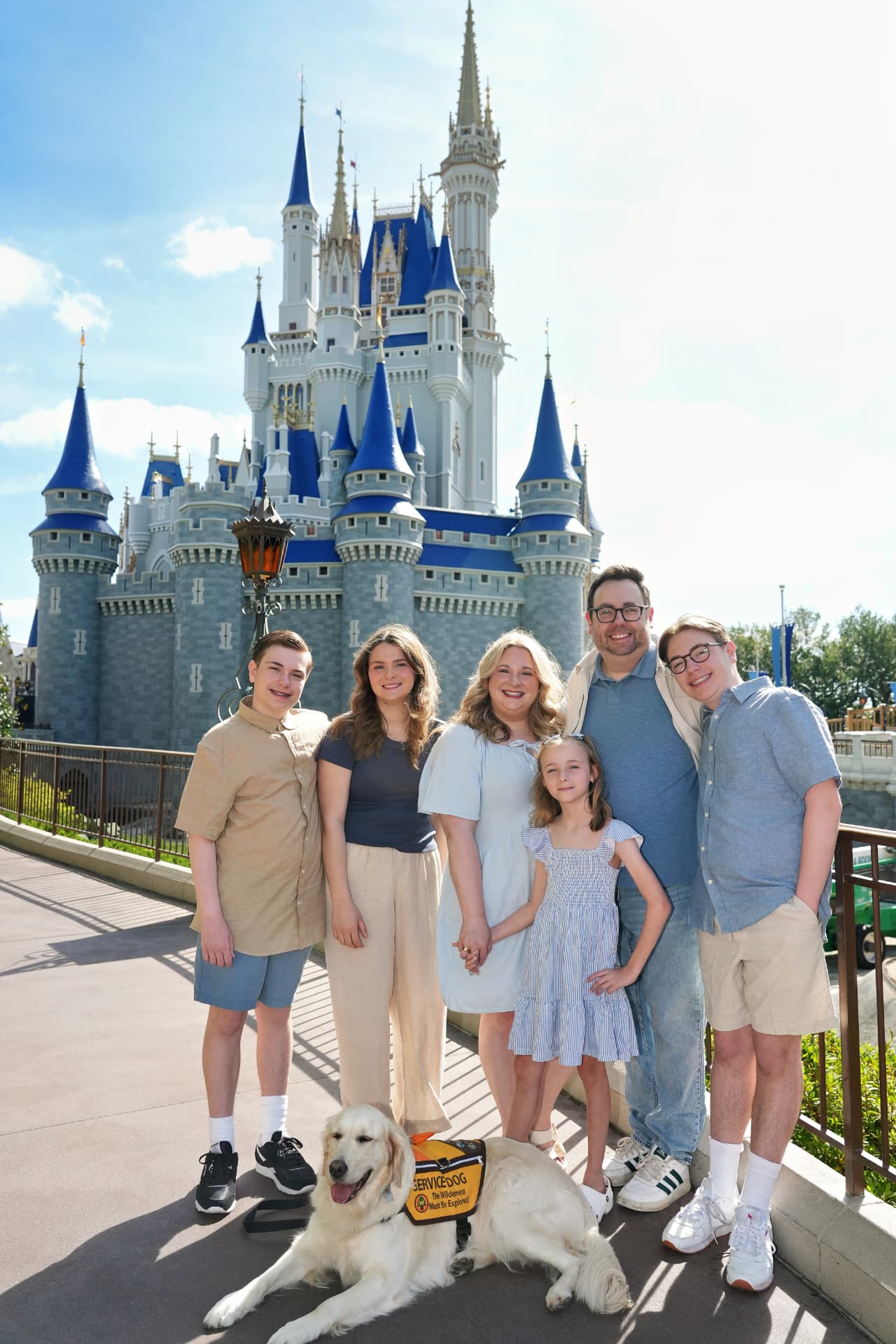 Jamie Thomas with her family and service dog in front of Cinderella Castle